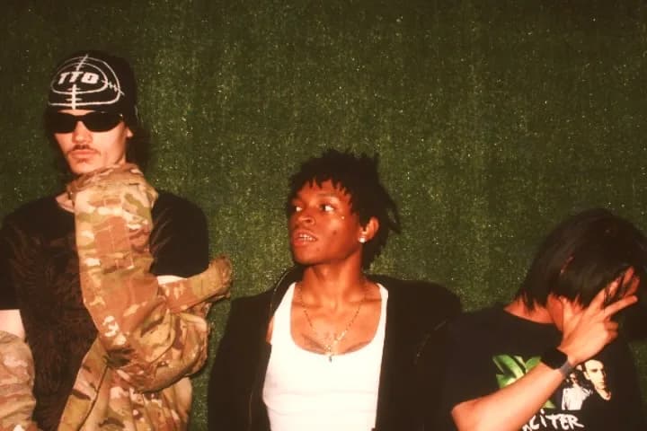 Three performers lined up against a dark green wall