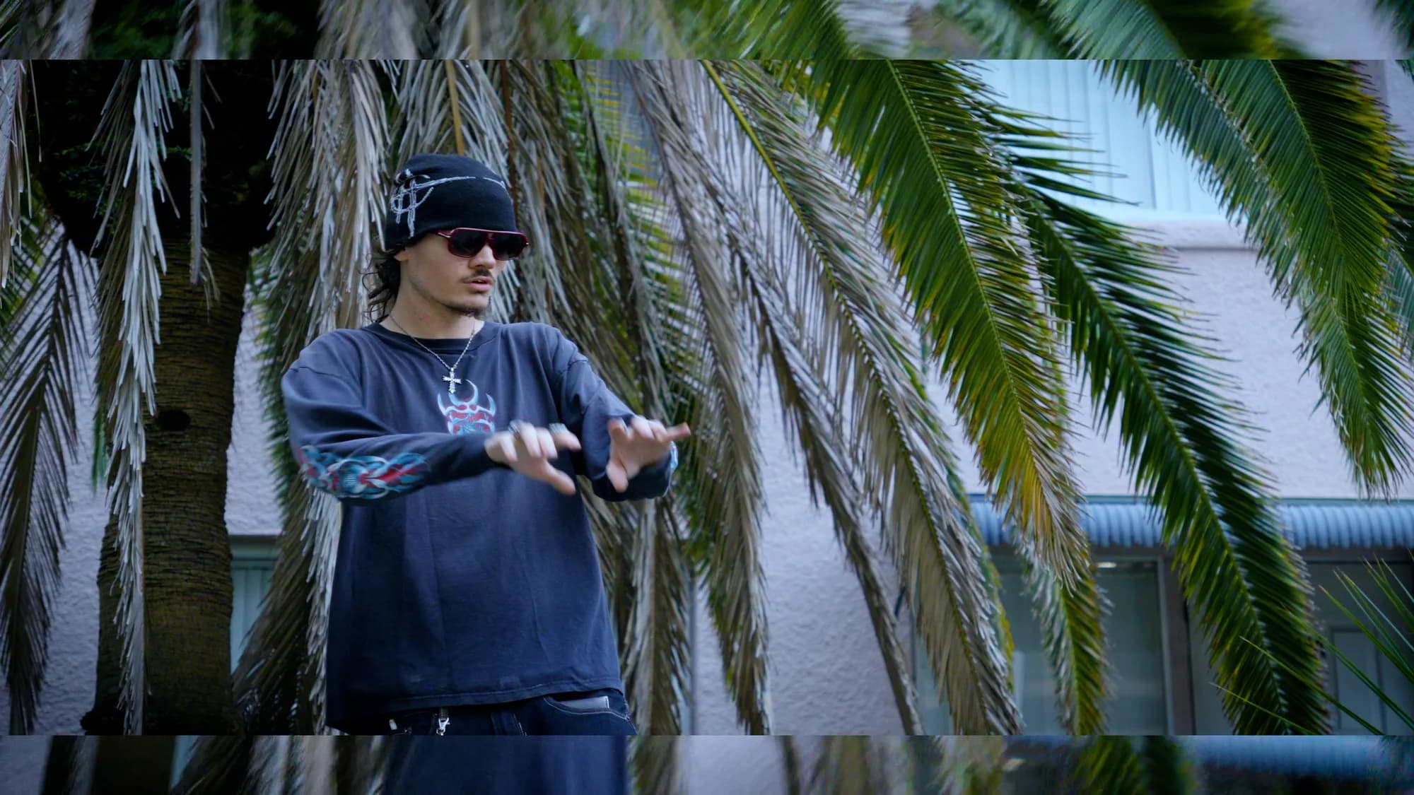 Outdoor portrait among palm fronds, wearing sunglasses and a dark bandana