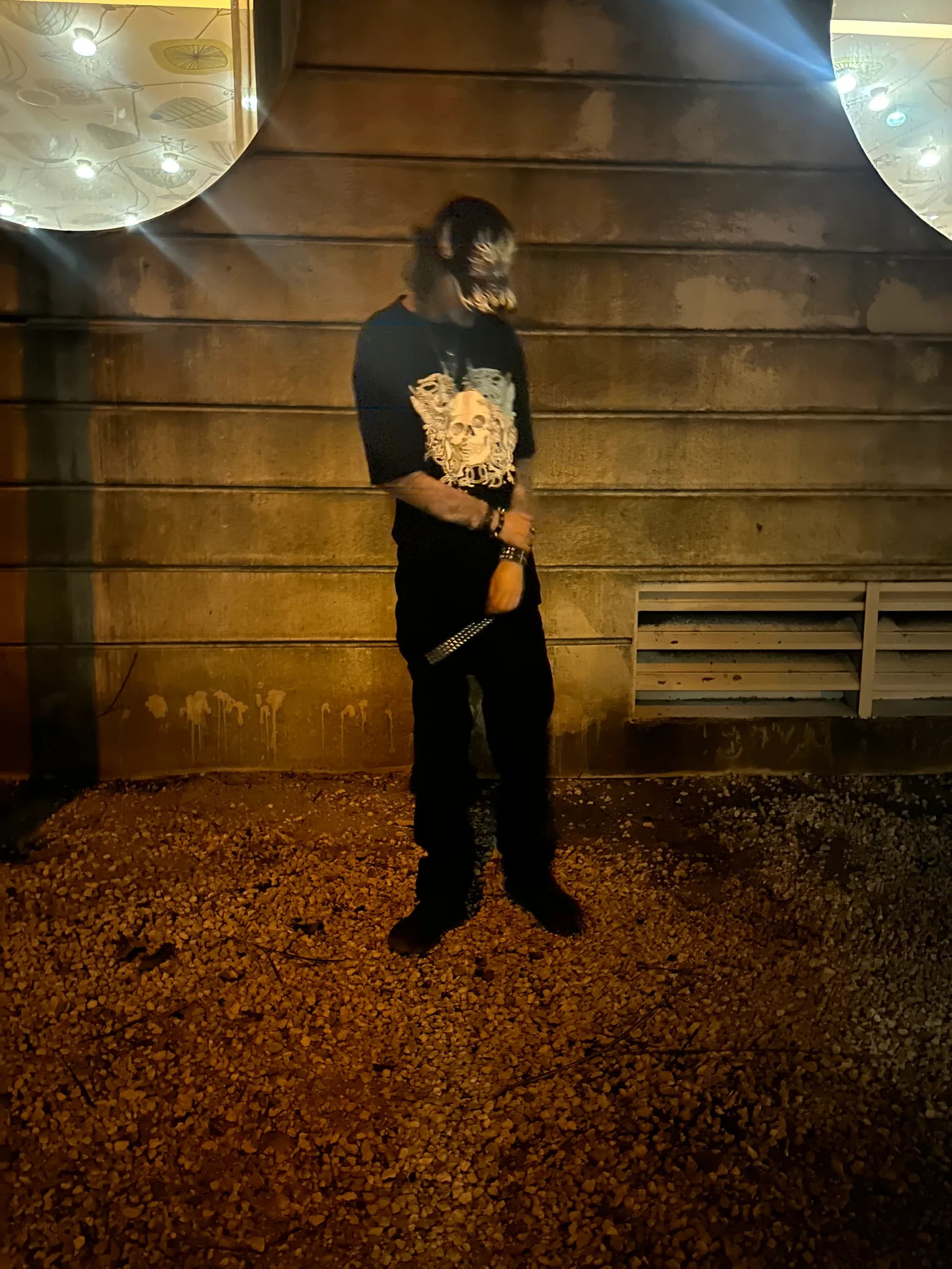 Standing on gravel at night against a concrete wall between two glowing lights